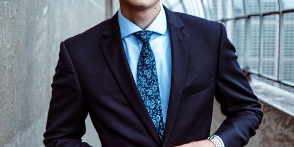 A man in a black suit and blue floral tie standing confidently.