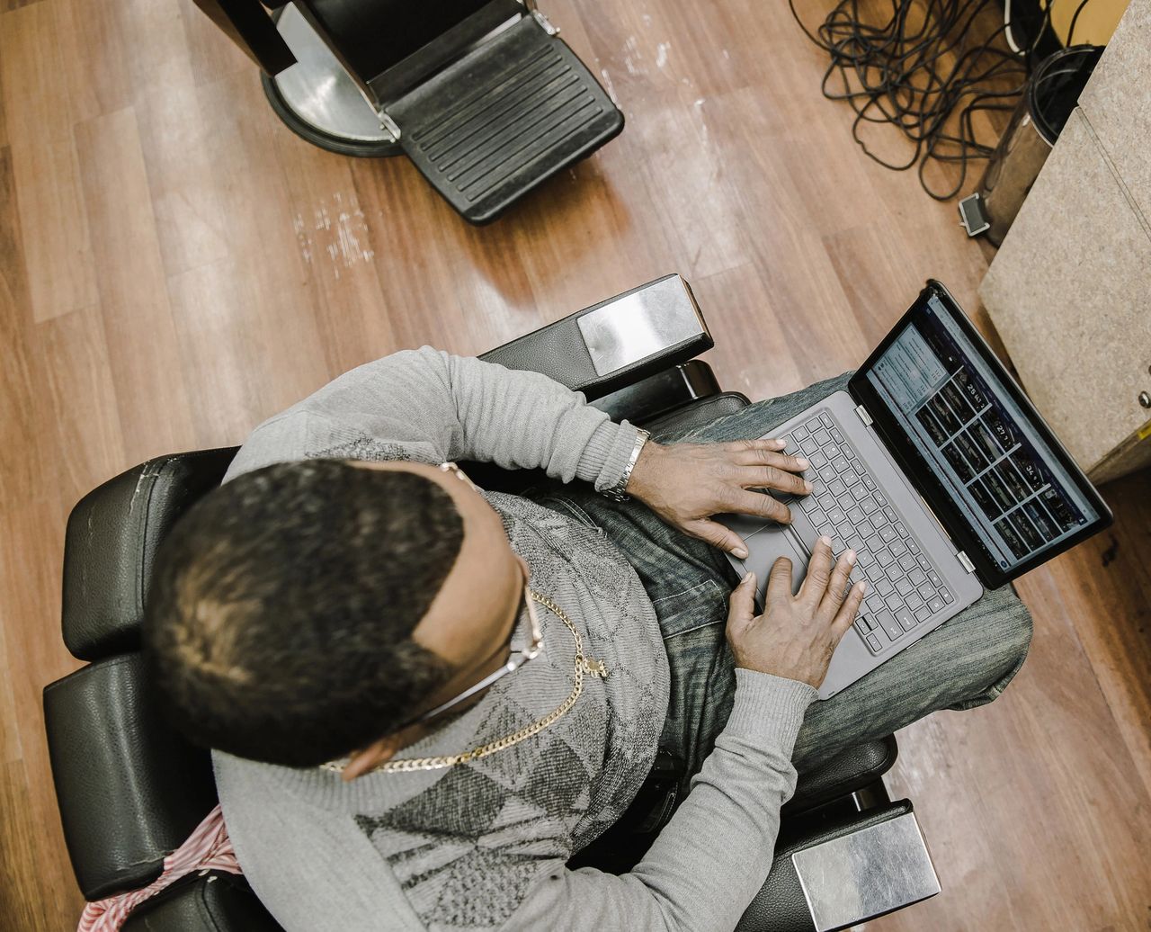 Person sitting in a barber chair using a laptop to manage blog writing projects, reflecting the efficiency of outsourcing content creation.