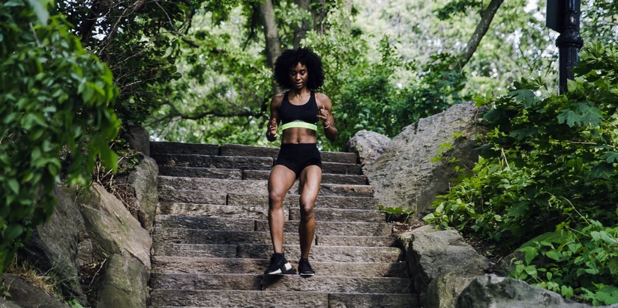 Woman jogging down stone stairs in a lush green park.