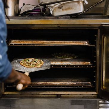 Staff member preparing pizza in a gas oven