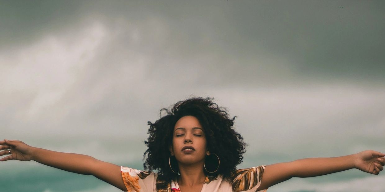 Woman with arms outstretched and eyes closed under a cloudy sky.