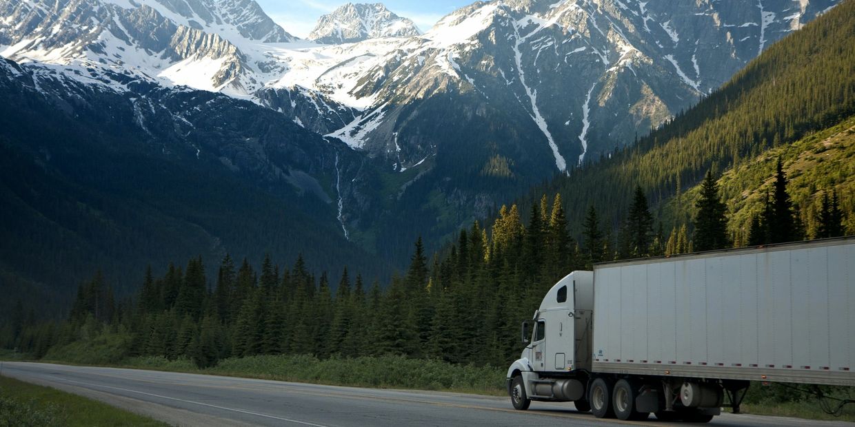 A large white truck driving on a road with snow-covered mountains in the background.