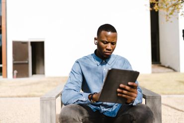 Man sitting outside reading a tablet.