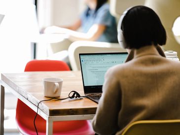 person with headphones on a laptop with cup