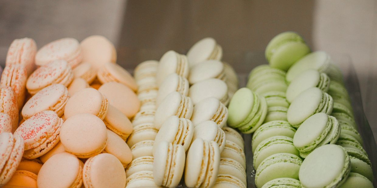 Rows of pastel-colored macarons in peach, white, and green hues.