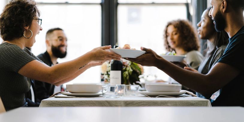 men and women gathered at a table handing each other plates and having dinner