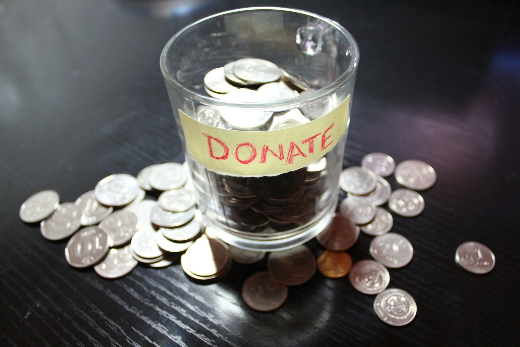 small glass with a label that says "donate", there are coins in the glass and around it