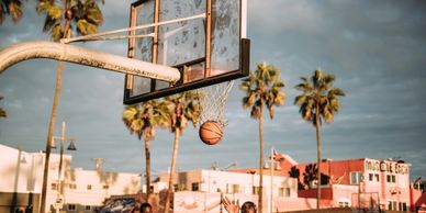 A basketball going through an outdoor hoop with palm trees in the background.