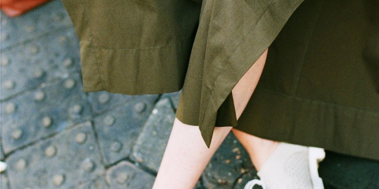 Person wearing olive green pants and white sneakers sitting on a textured surface.