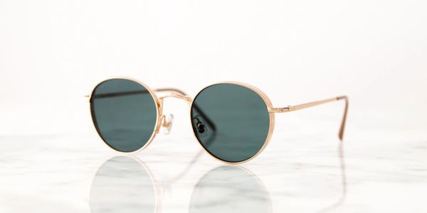 Round sunglasses with gold frames and dark lenses on a white surface.