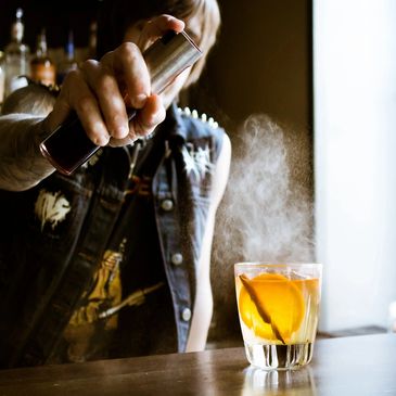 A punk rock, grudge bartender spritzing an old fashioned