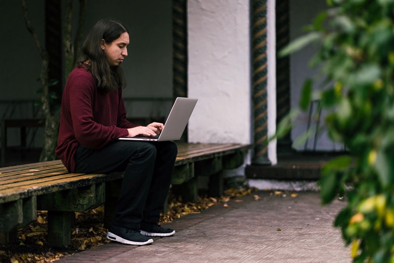 Person using a laptop on a wooden bench, emphasizing digital engagement and remote work in a serene outdoor setting, relevant to media planning and campaign optimization.