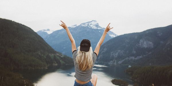 Woman sitting on hill in enjoying the view of mountains with her hands up in the air celebrating.