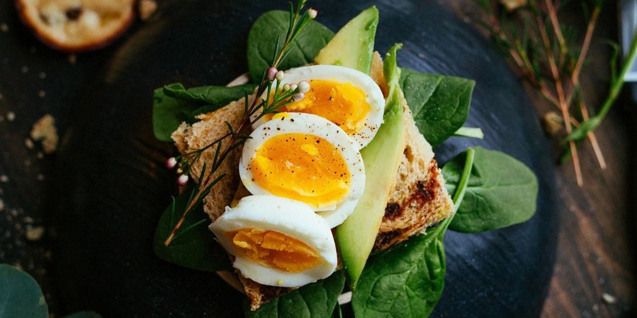 Open sandwich with boiled egg, avocado, and spinach on toasted bread.
