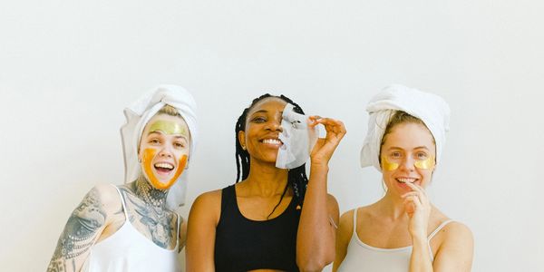 three women standing together with skin care products on face 