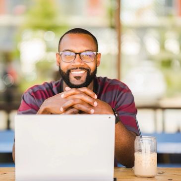 Man looks happy as he sits at his desk, hands crossed with the computer open. 