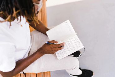 Person writing in a notebook while sitting on a bench.