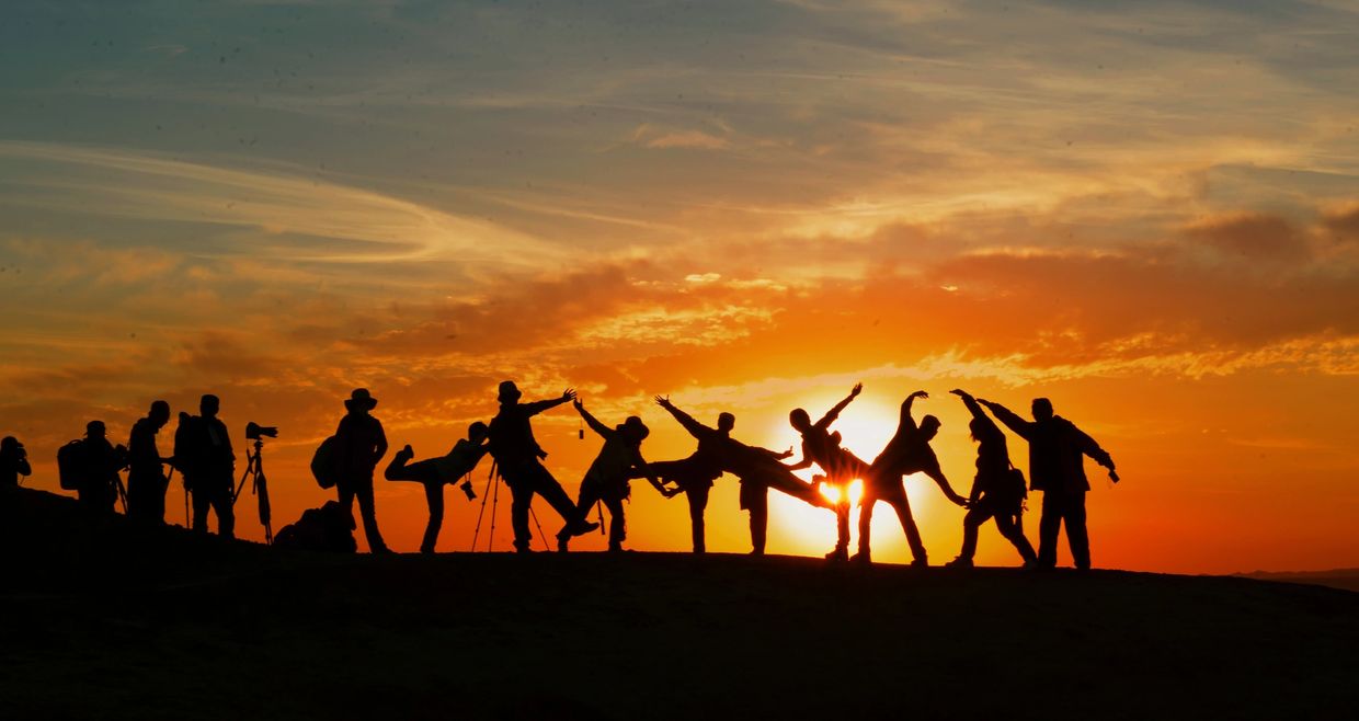 Silhouettes of a group enjoying sunset with playful poses on a hill.