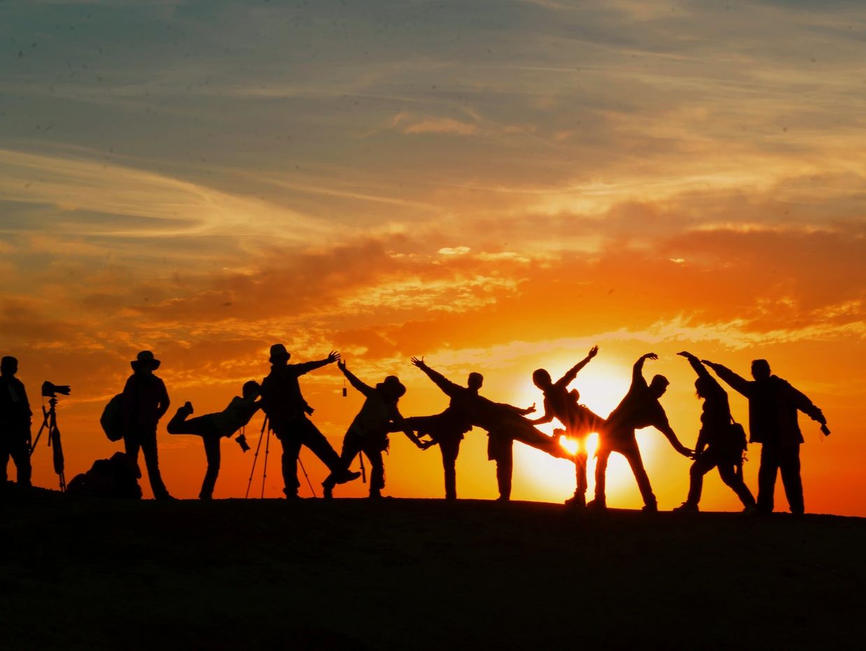 Silhouetted group posing dynamically at sunset on a hilltop.