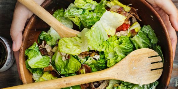 Fresh green salad in a wooden bowl with wooden utensils.