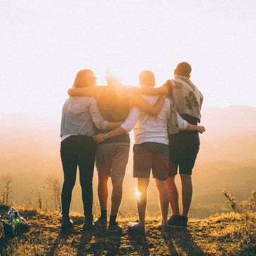Four friends embracing and watching sunset on a hilltop.
