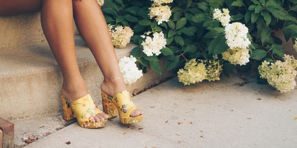 Snappy looking high heeled sandals next to a blooming, white petaled hydrangea bush.