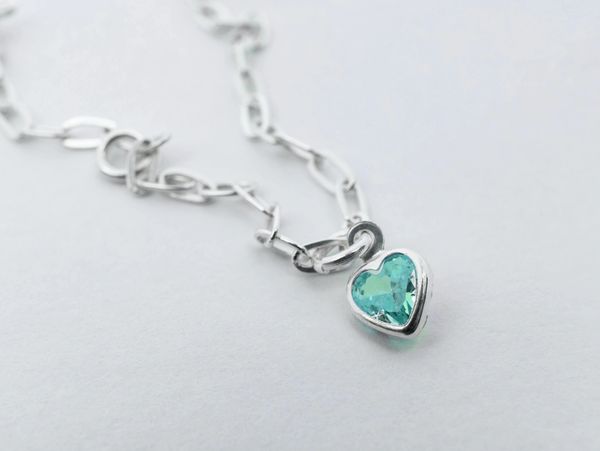 Silver chain necklace with a heart-shaped teal gemstone pendant.