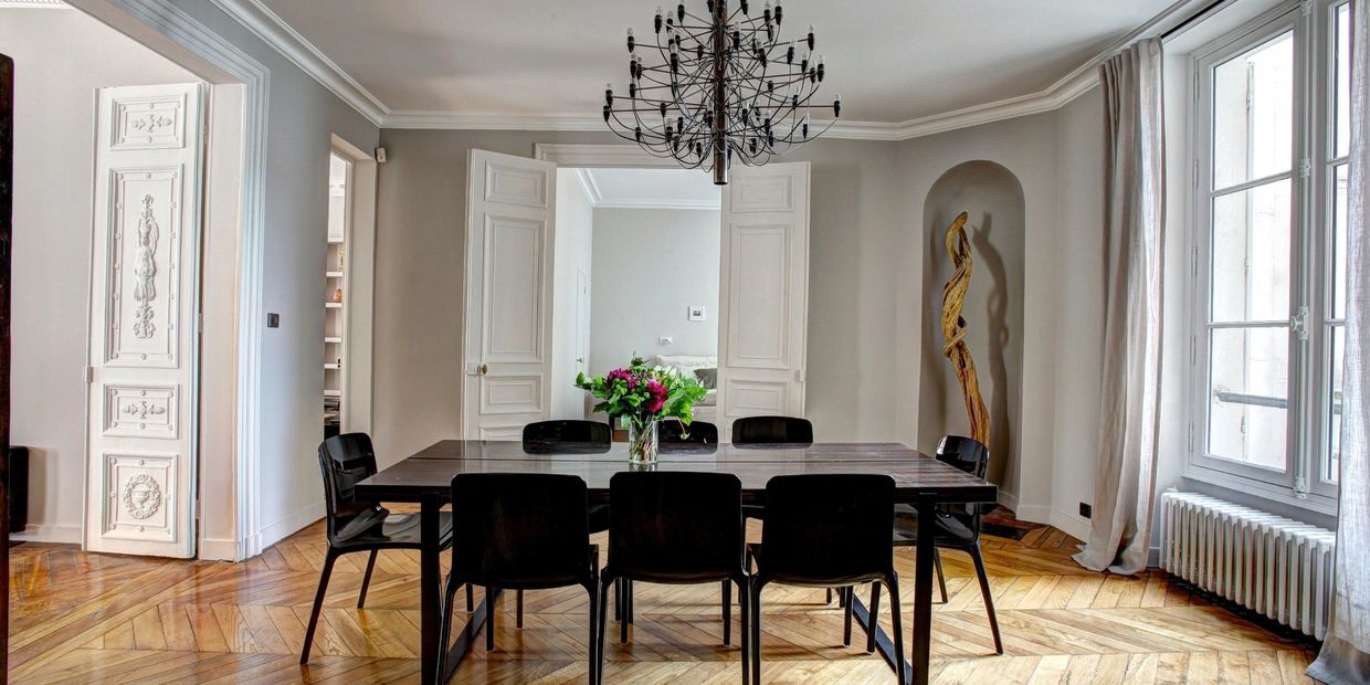 Modern dining room with black chairs, wooden floor, and large windows.