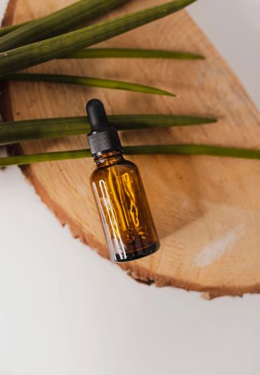 Brown dropper bottle on wooden slab with green leaves.