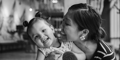 A joyful mother affectionately holding her smiling toddler indoors.