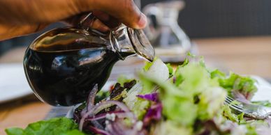 Green salad with onions on plate and hand pouring out a deep red type of dressing