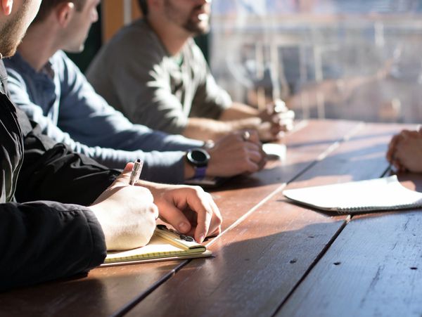 People writing notes during a meeting at a wooden table.