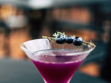 A vibrant purple cocktail garnished with blueberries on a skewer.