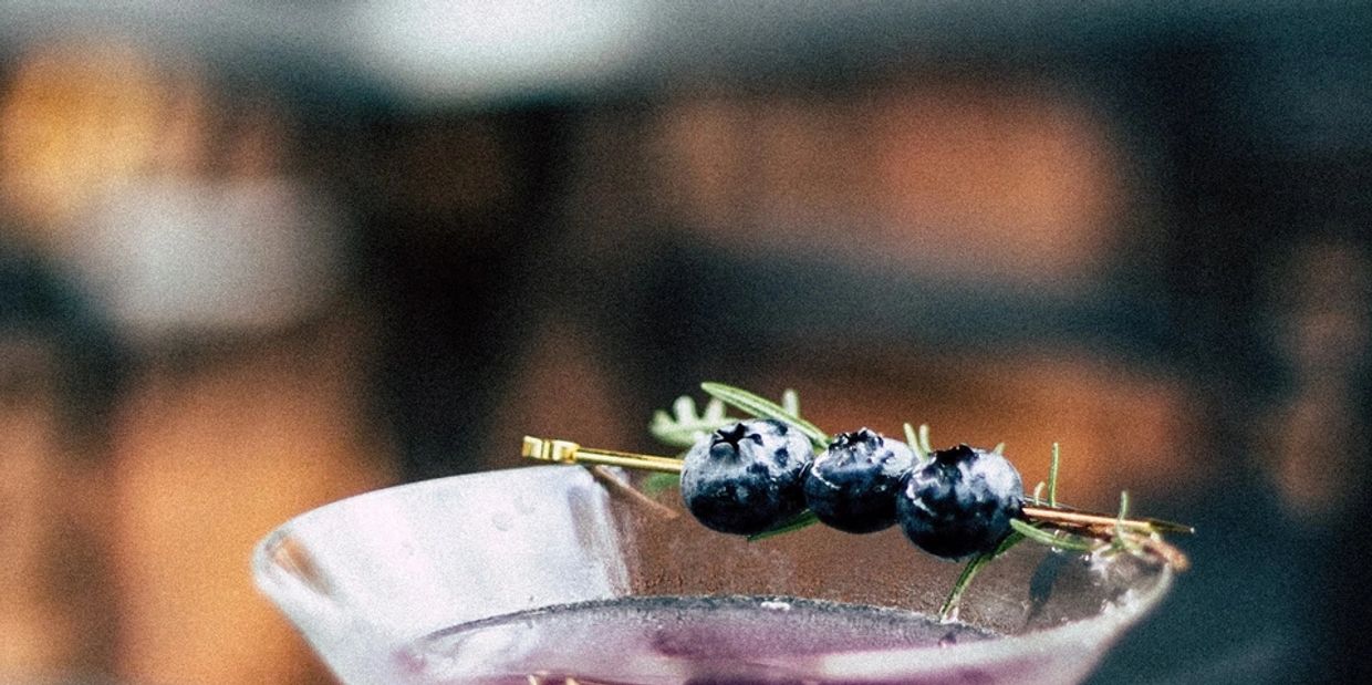 Close-up of a cocktail garnished with blueberries and rosemary.