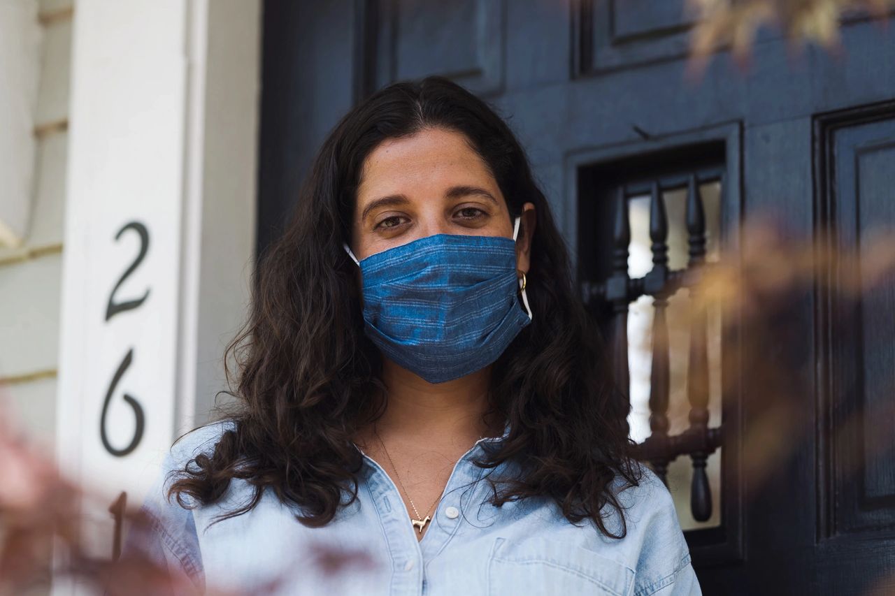 Lady stands outside of her home with her facemask on for protection from harmful airborne substances.