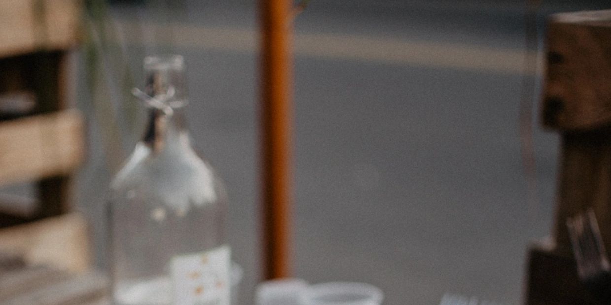 Empty clear glass bottle and cups on a wooden table outdoors.