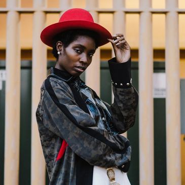 Confident woman in a red hat and patterned jacket posing outdoors.