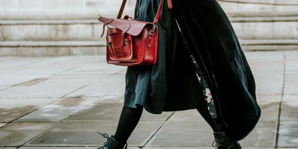 Person walking with a red leather satchel and black boots on a stone pavement.
