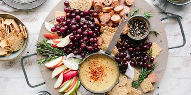A charcuterie board with cheese dip, grapes, crackers, apple slices, and sausage.