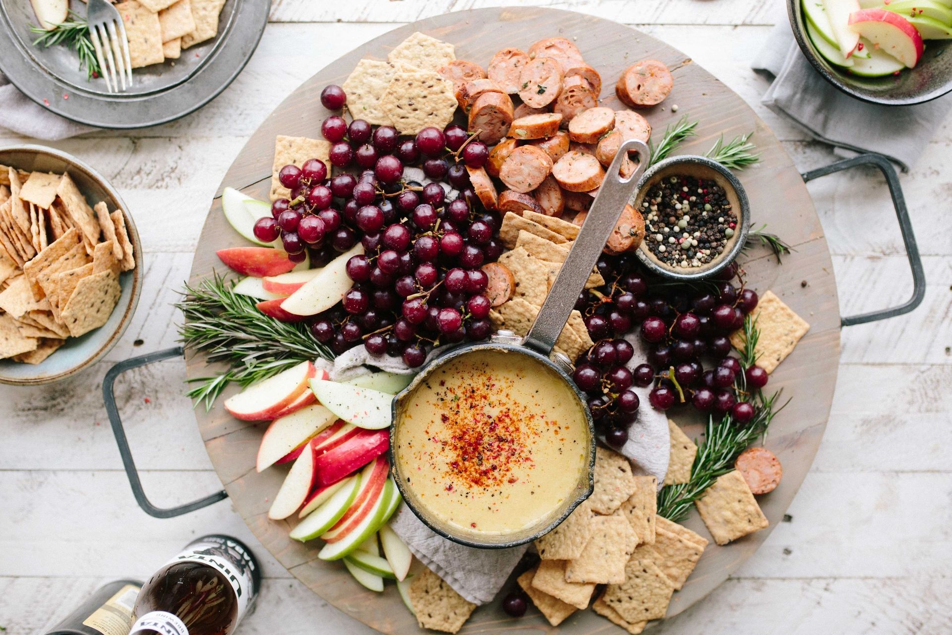 A charcuterie board on a table surrounded by small bowls of crackers and fruit