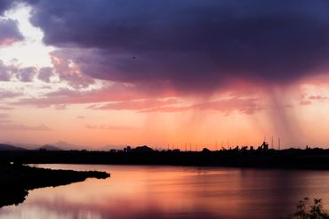 Sunset with rain clouds over a calm lake reflecting orange and purple hues.