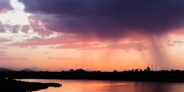 Sunset with vibrant orange sky and distant rain over a calm water body.
