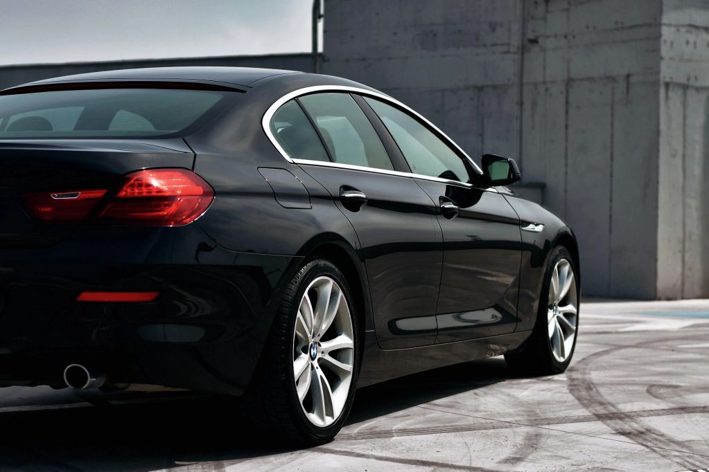 Black luxury sedan parked near a concrete wall.