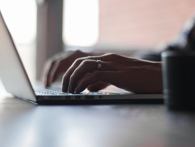 Close-up of hands typing on a laptop keyboard with a cup nearby.