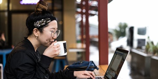 A Women sipping coffee while entering data on her laptop