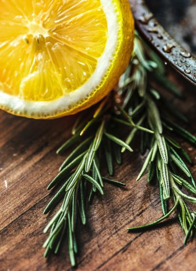 Close-up of lemon slice and rosemary sprigs on wooden surface.