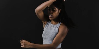 A woman in a gray sleeveless top dances with expressive movements against a black background.