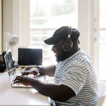 A man is typing on a laptop while wearing headphones. He is smiling