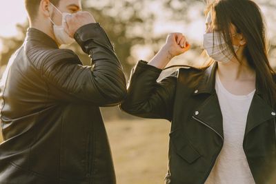 Two individuals giving elbow bump while wearing face coverings.