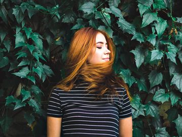 Young woman with red hair stands in front of green ivy.